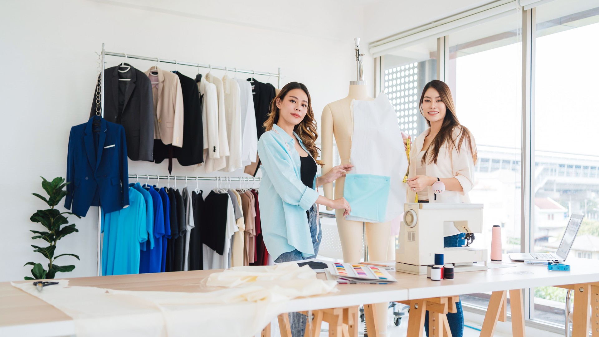 Asian female fashion designer or tailor with assistance preparing cut paper fabric pattern. Dressmaker working and designing new fashion collections for customers in atelier tailor workshop.