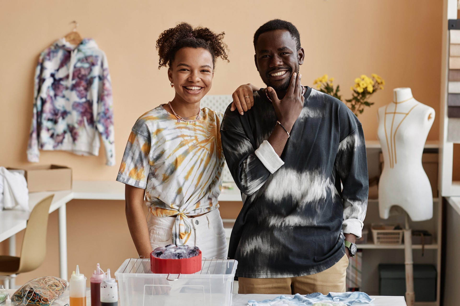 Happy young male and female designers in tie dye t-shirts looking at you
